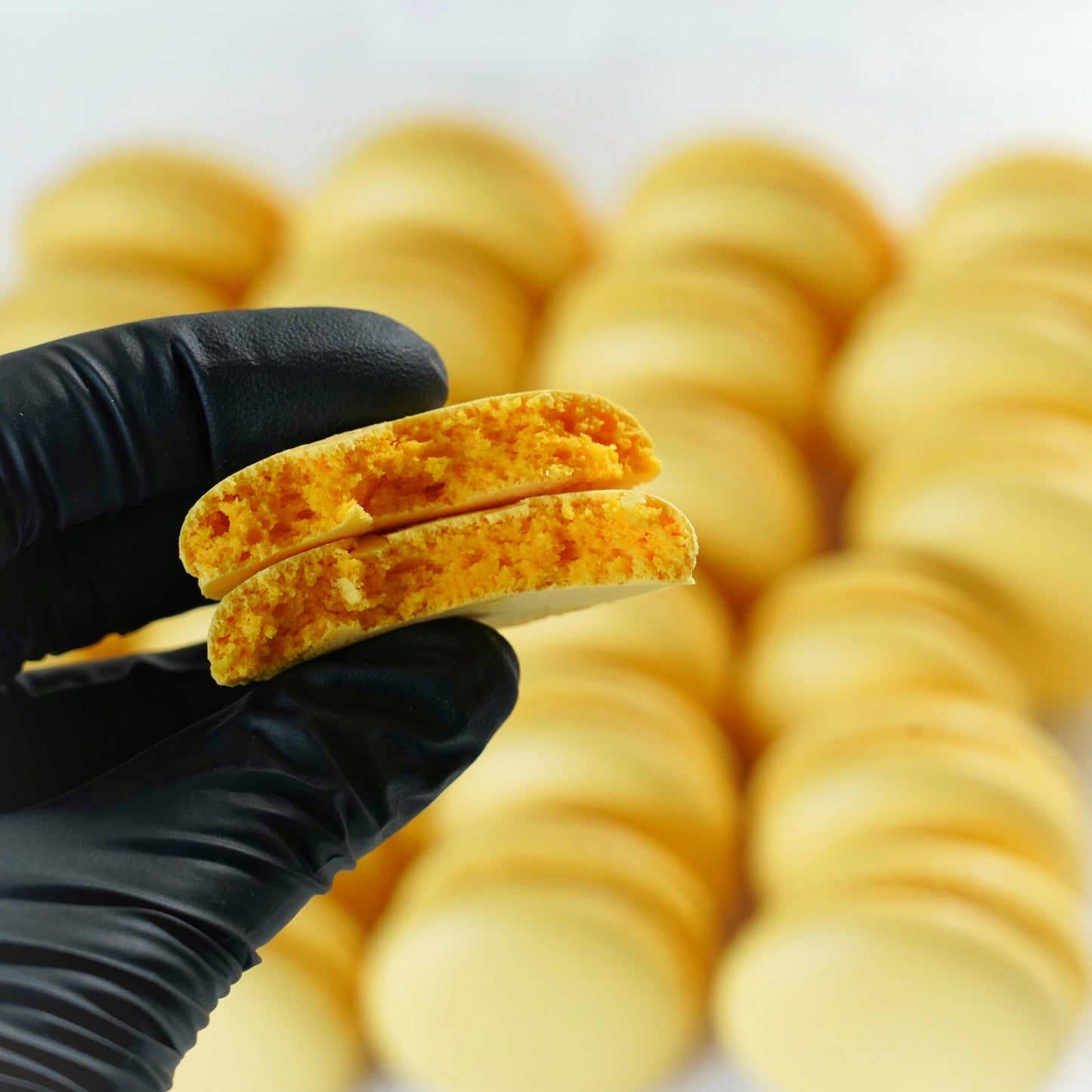 Hand holding a perfect macaron shell with more shells in the background