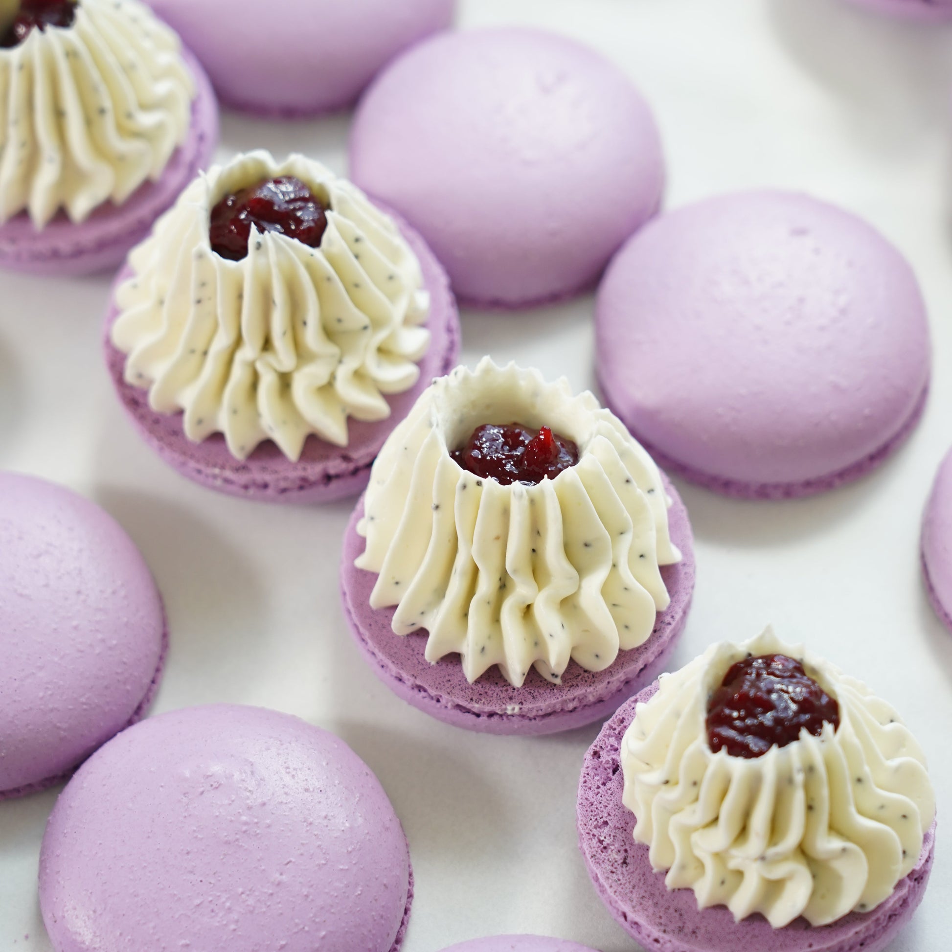 Purple macarons with cream and a red berry filling on a white surface