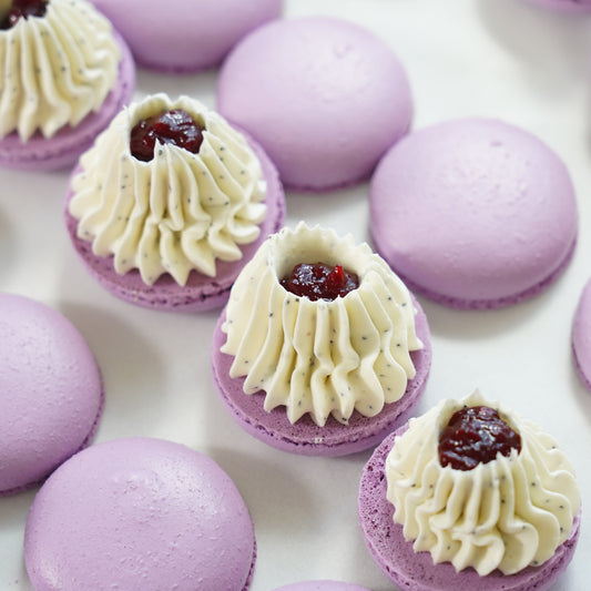 Purple macarons with cream and a red berry filling on a white surface