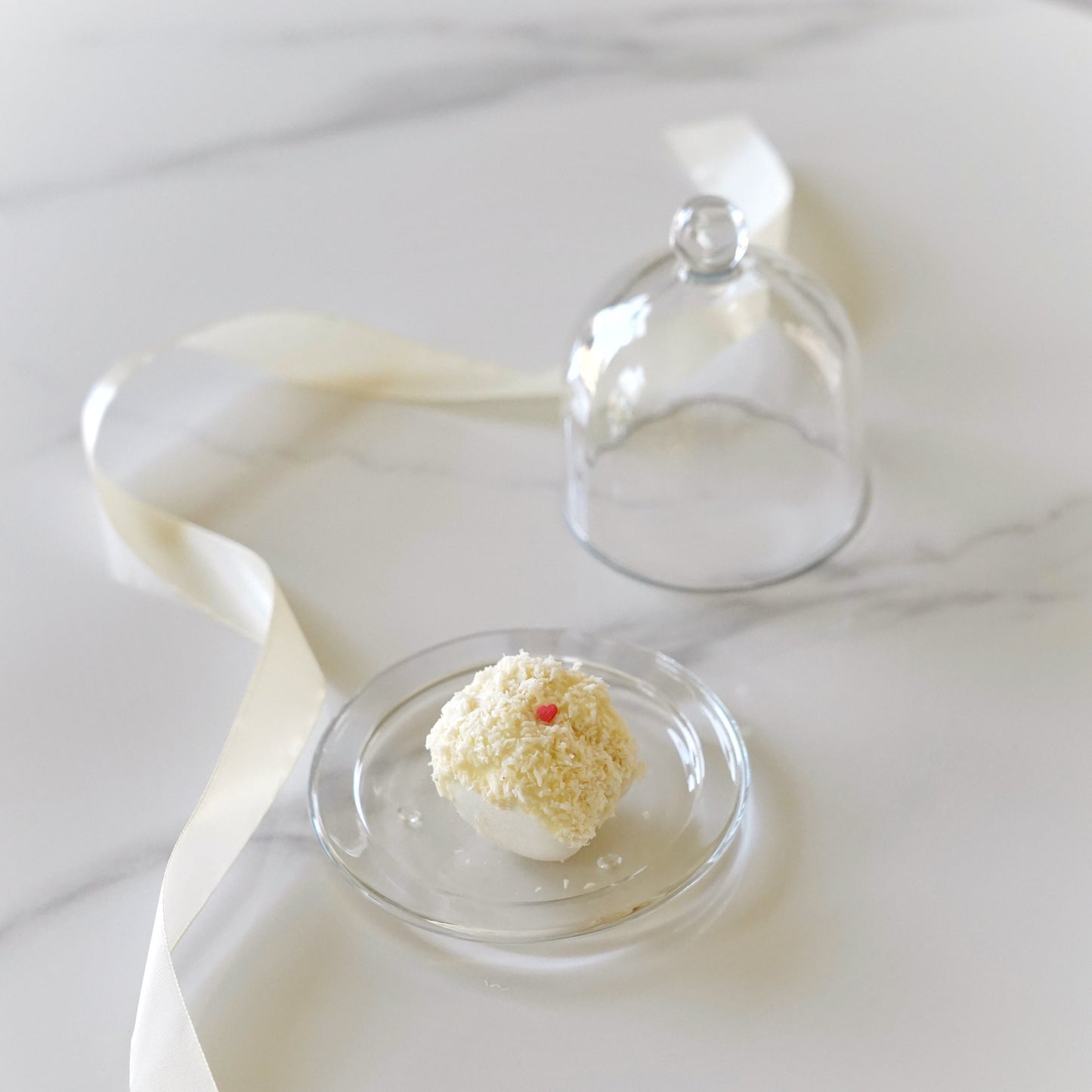 Small dessert in a clear glass dome on a white fabric background
