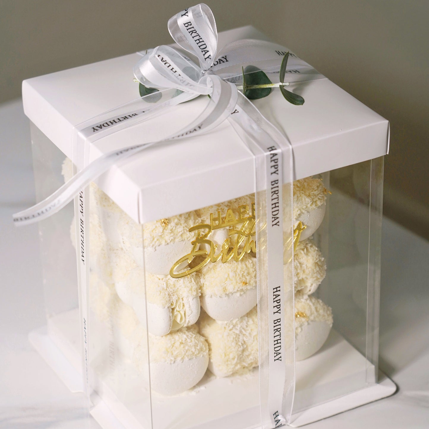 Gift box with white macarons cake and a gold 'Happy Birthday' message on a white background